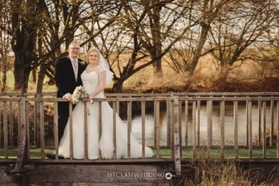 Bride and groom smiling on wooden bridge outdoors.