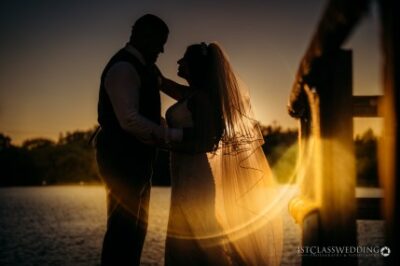 Couple embracing at sunset by lake, wedding silhouette.