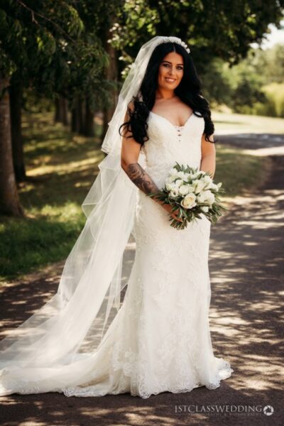 Bride in lace dress holding bouquet outdoors.