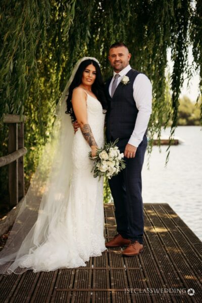 Bride and groom posing by lake under willow tree