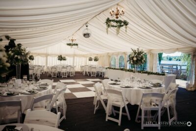 Elegant marquee wedding setup with white drapery and tables.