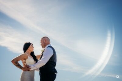 Couple embracing at outdoor wedding under blue sky.