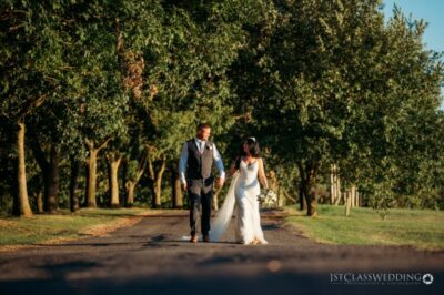 Couple walking on tree-lined path at wedding.