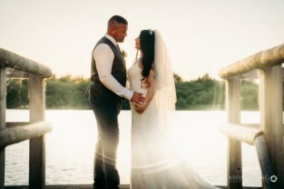Bride and groom holding hands at sunset by lake
