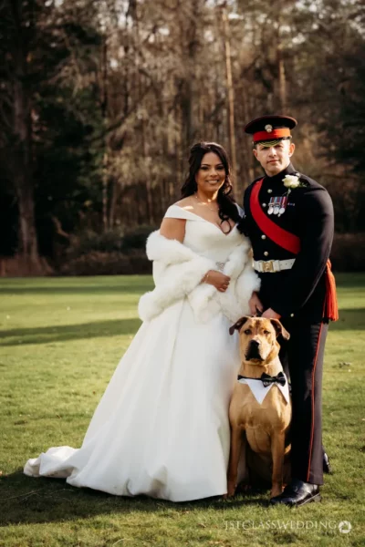 Bride, uniformed groom, and dog at wedding outdoors.