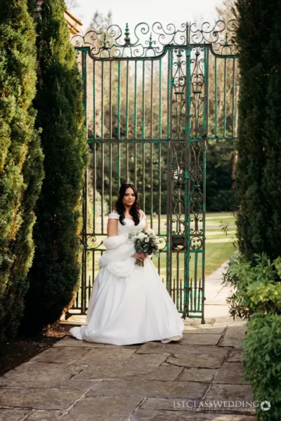 Bride holding bouquet at ornate garden gate.