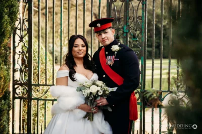Bride and groom in military uniform at gate.