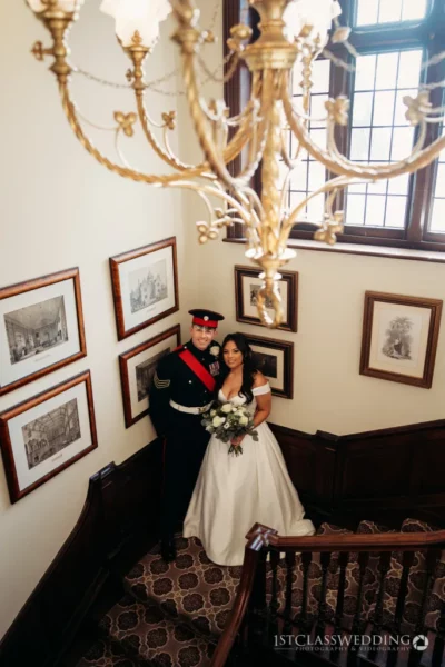 Military groom and bride on staircase with chandelier.