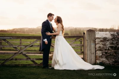 Couple embracing by gate at sunset wedding.