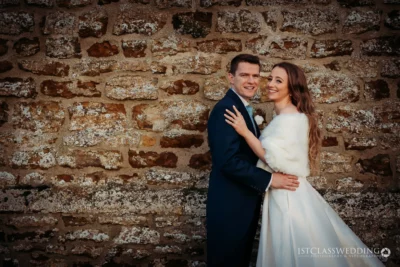 Couple embracing at rustic stone wall on wedding day.