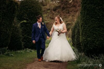 Bride and groom walking together in garden.