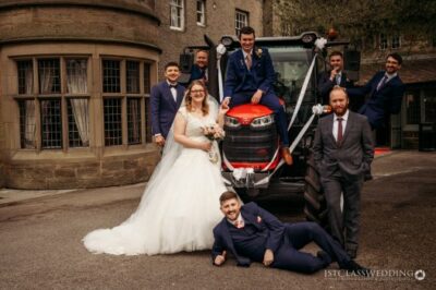 Bride, groom, and friends with tractor at wedding venue.