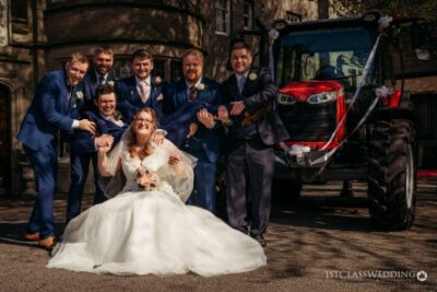 Wedding party posing with tractor outside historical venue.