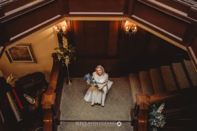 Bride with bouquet sitting on elegant staircase.