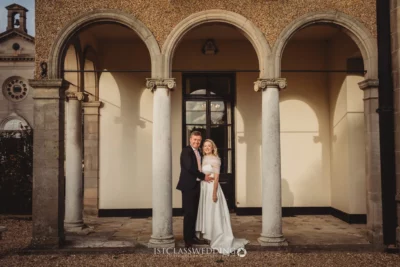 Couple posing at historic building entrance, wedding day.