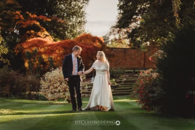 Couple holding hands in autumn wedding setting.