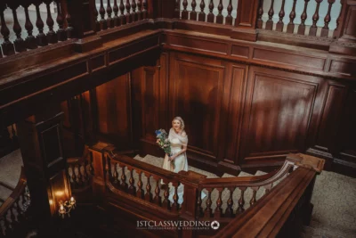 Bride posing on grand wooden staircase with bouquet.