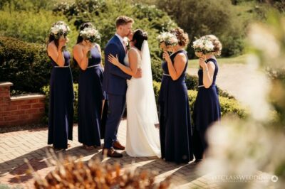 Bride and groom kissing, bridesmaids in navy, sunny garden wedding.