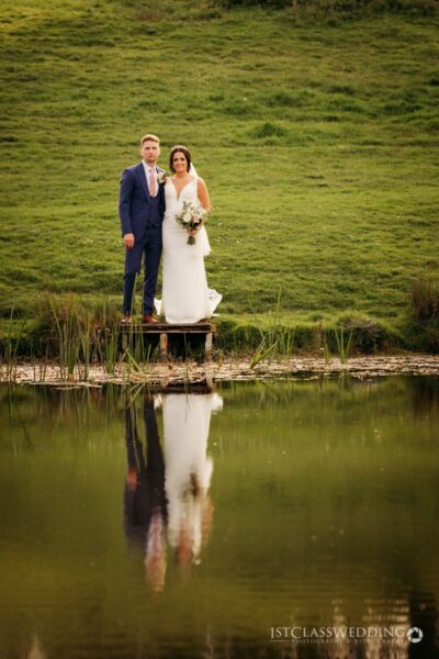 Wedding couple standing by pond with reflection
