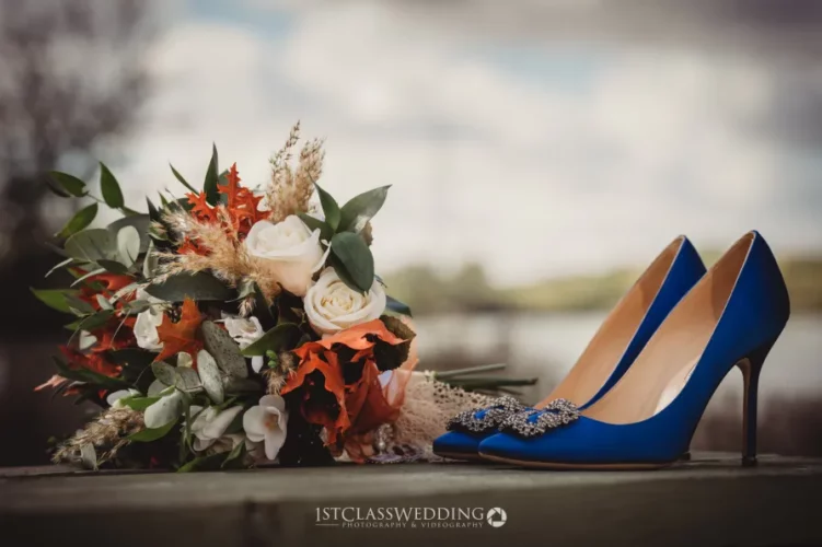 Bridal bouquet and blue high heels on wooden surface.