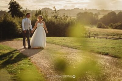 Couple walking hand in hand at sunset countryside wedding.