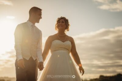 Couple holding hands in wedding attire at sunset