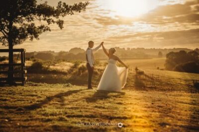 Couple holding hands in sunset-lit countryside wedding scene.