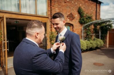 Groom getting boutonniere pinned outdoors at wedding.
