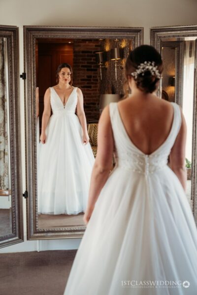 Bride in white dress admiring reflection in elegant mirror.