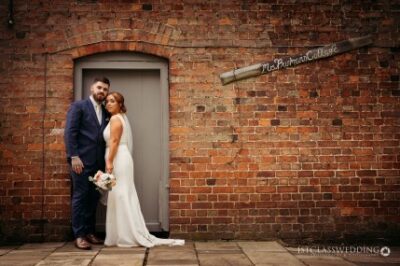 Bride and groom posing by brick wall.