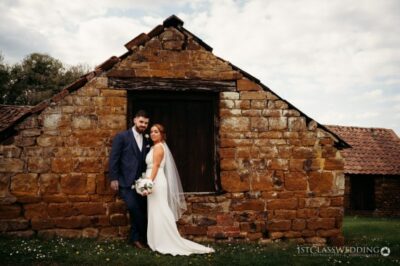 Couple poses at rustic stone barn wedding venue.