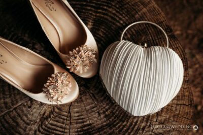 Bridal shoes and heart-shaped handbag on wooden stump.