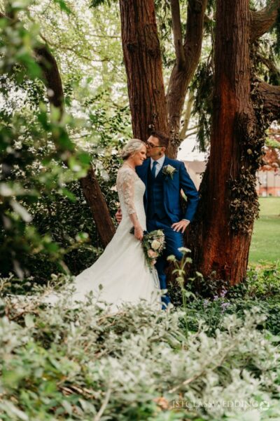 Bride and groom embracing by trees.