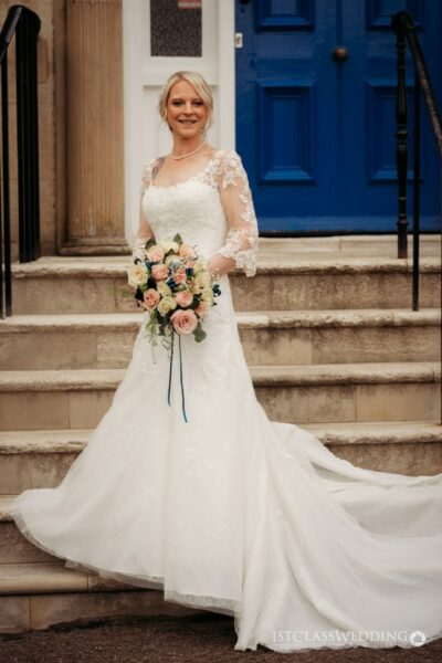 Bride in lace gown with pastel bouquet, blue door backdrop.