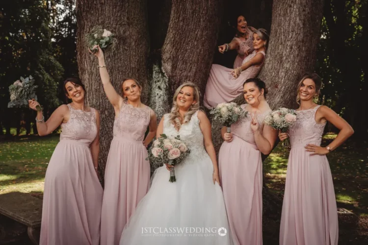 Bride and bridesmaids with bouquets, posing by a tree.