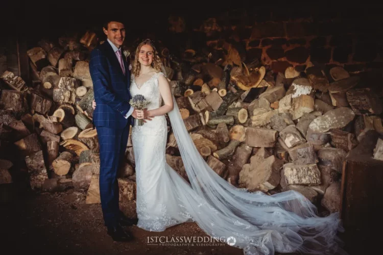 Bride and groom posing with firewood backdrop.