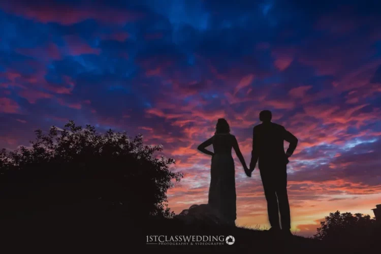 Couple silhouette against vibrant sunset sky.