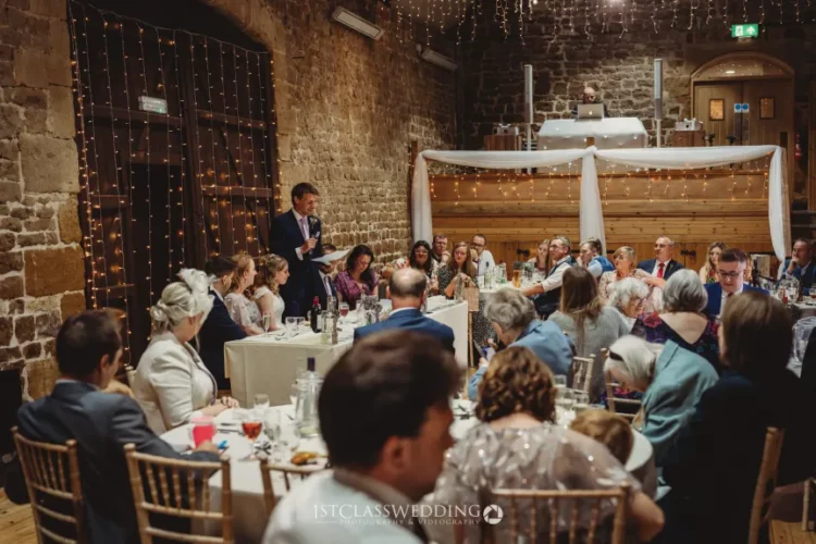 Wedding speech at rustic venue with guests listening.
