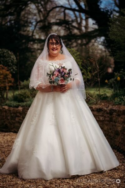 Bride in gown with bouquet, outdoor wedding setting.