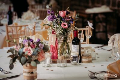Elegant wedding table setting with floral arrangement and wine.