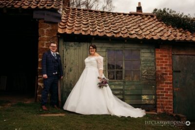 Bride and groom posing by rustic barn.