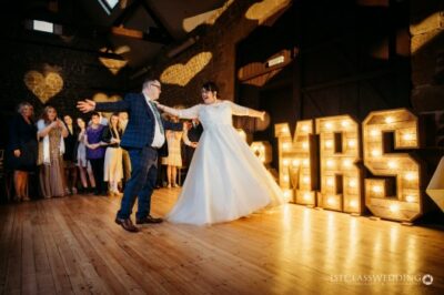 Couple's first dance at wedding with illuminated 'MR & MRS' sign.
