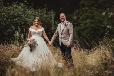 Bride and groom holding hands in a meadow.