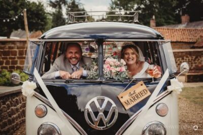 Couple celebrating in vintage VW camper van with "Just Married" sign.