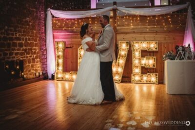Bride and groom first dance with illuminated 'LOVE' sign.