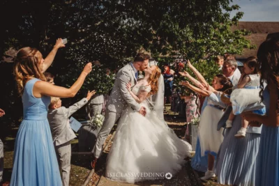 Couple kissing, confetti thrown, at sunny outdoor wedding.