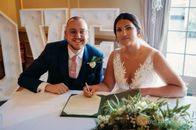 Bride and groom signing wedding register, smiling.