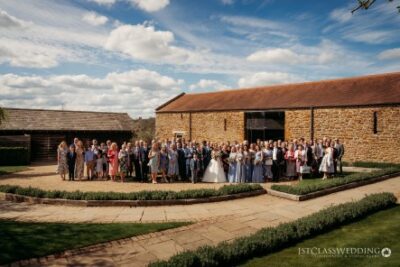 Wedding guests gathered outside stone venue on sunny day.