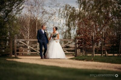 Bride and groom walking on path near wooden gate.
