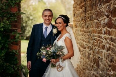 Bride and groom smiling by brick wall at wedding